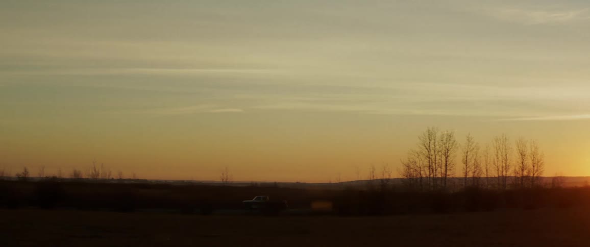 A truck drives across the landscape as the sun sets