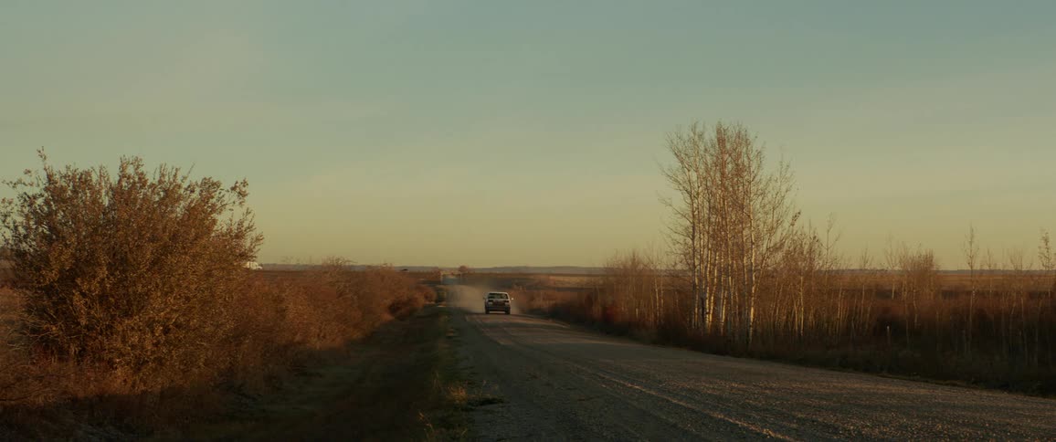A pickup truck drives down a gravel road and kicks up dust