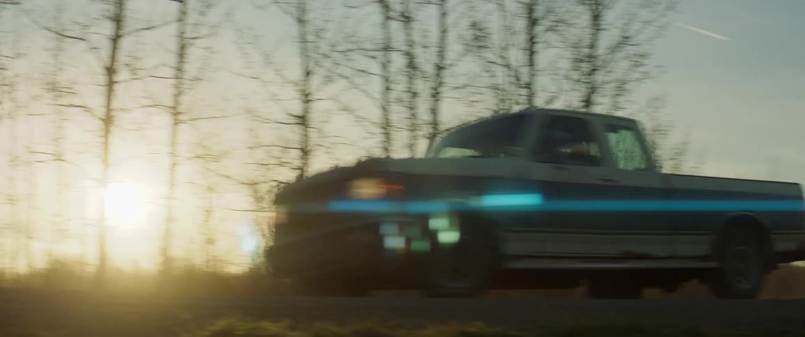 Old pickup truck with its headlights on traveling down a country road as the sun begins to rise