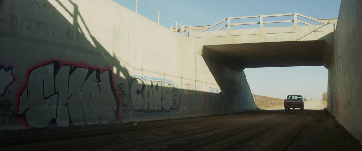 A pickup truck drives past a wall marked with graffiti