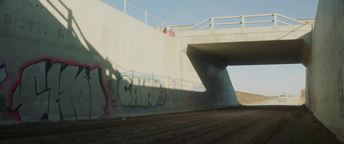 A pickup truck travels past graffiti on walls as a car travels above on an overpass