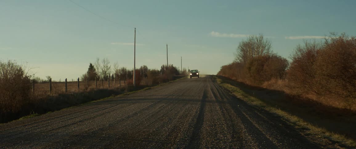 A pickup truck with headlights travels on a dirt road leaving a trail of dust