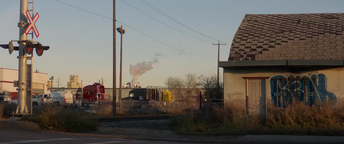 Semi and truck cross railroad tracks and graffiti touched building with damaged roof
