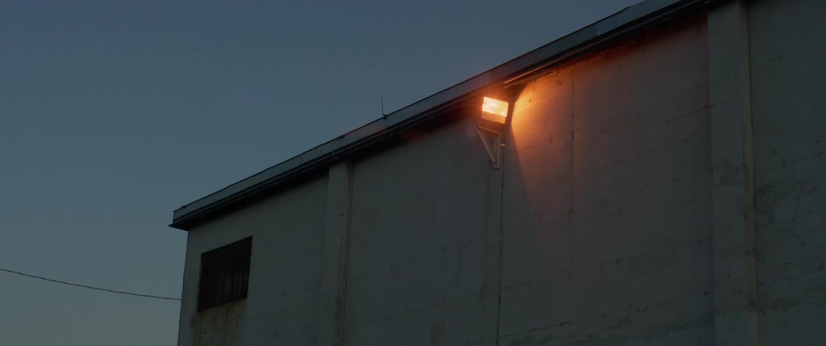 A lone security light burns on the outside of a building