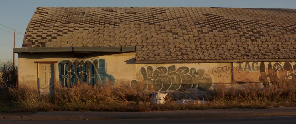 Traffic passes by an abandoned building marked with graffiti