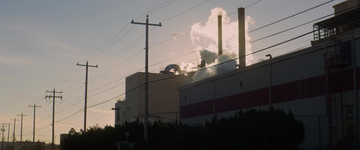 Smoke billows out of a factory as an airplane flies overhead