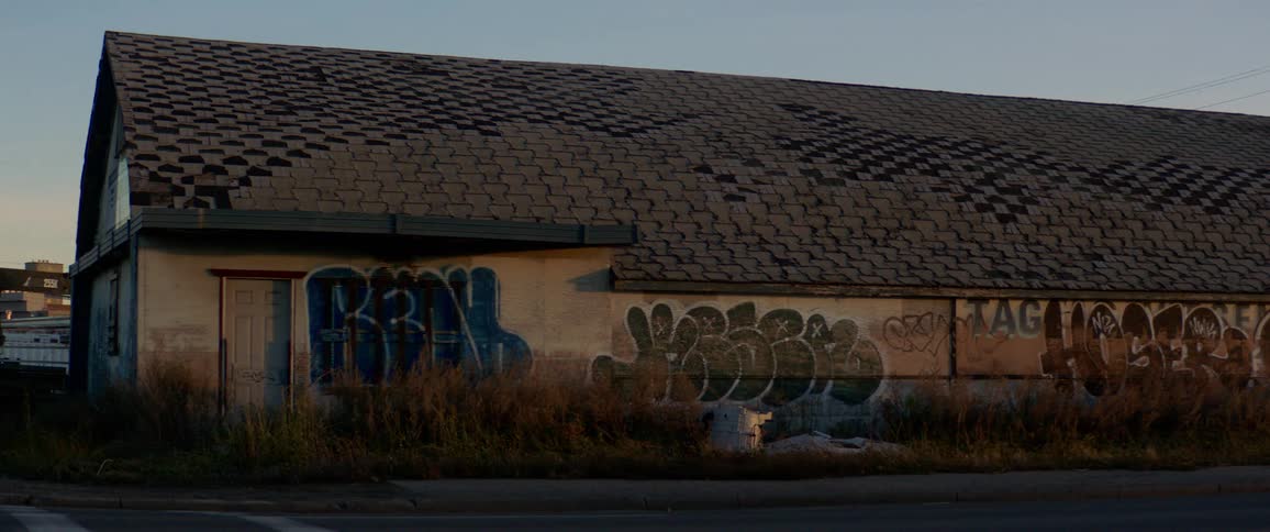 Traffic drives past graffiti covered building at dusk