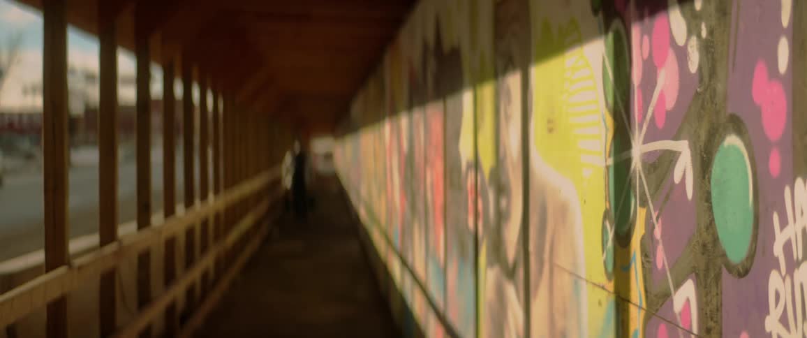 Artwork and graffiti line the walls of a covered walkway as a pedestrian walks