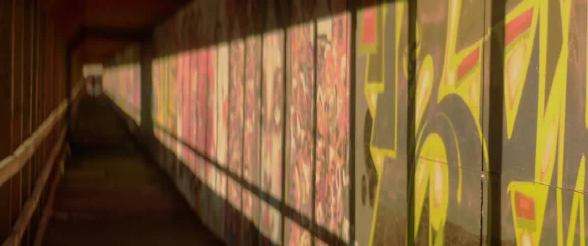Graffiti covers the wooden boards of a covered sidewalk in a city on a sunny day