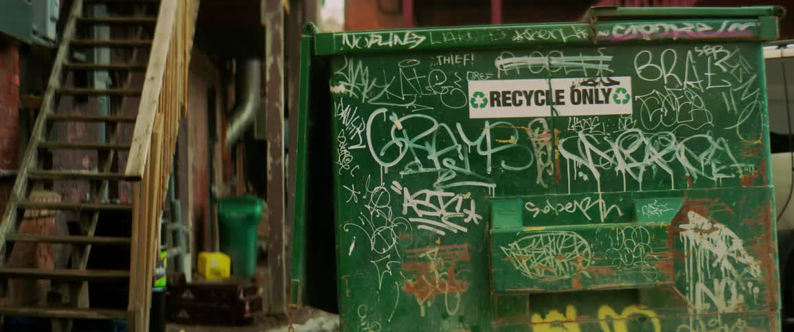 A recycle bin covered in graffiti sits next to a wooden staircase