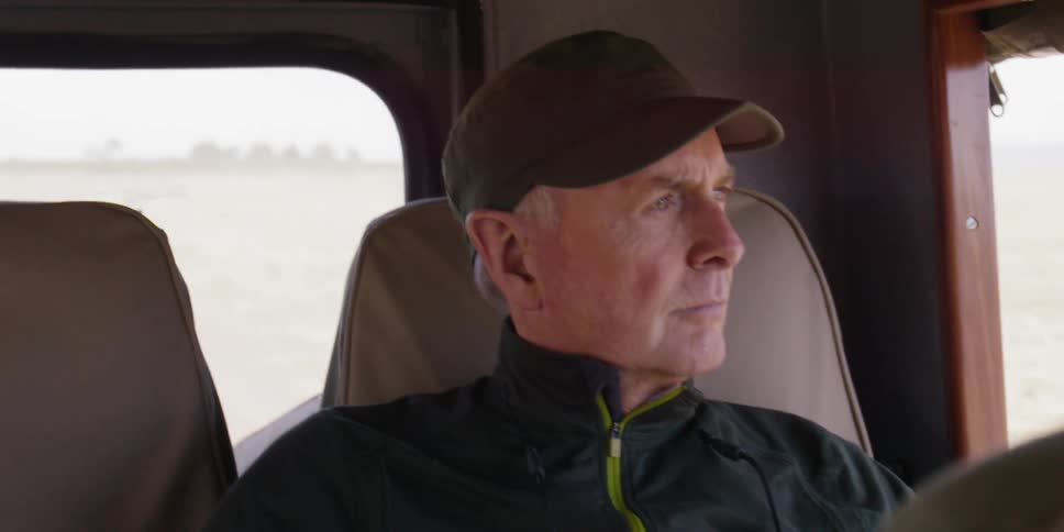 An elderly man looking out of a window as he travels down a road