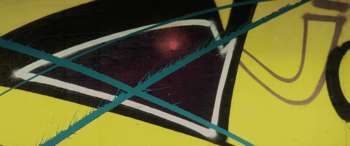 Graffiti made up of shapes lines and text are tagged onto a yellow wall