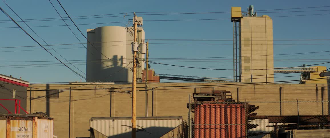 A semi travels past a building and shipping containers