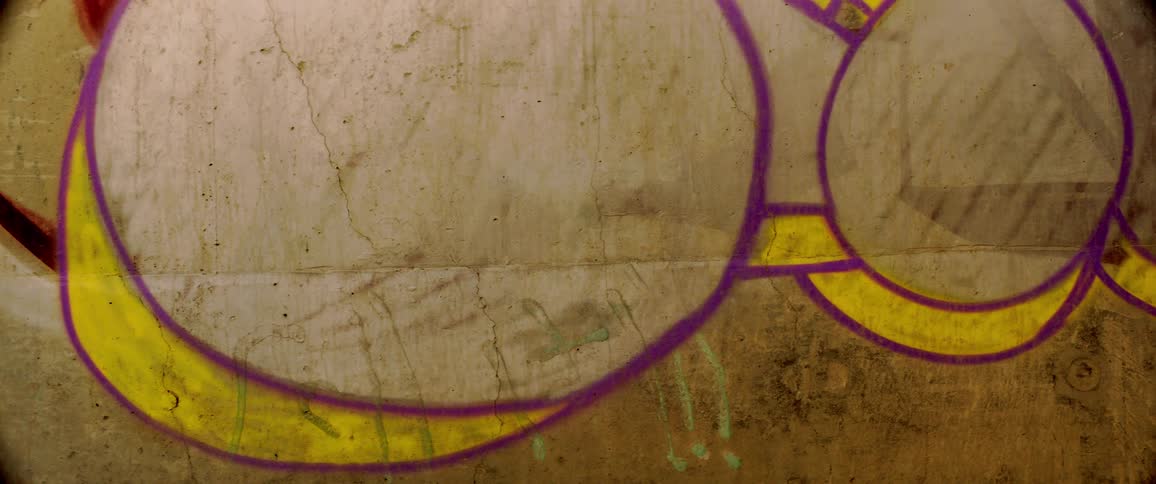 A dirty wall covered in purple and yellow spray paint