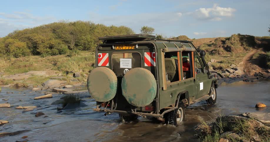 A small transport truck makes its way over the rocks of a small stream in the wilderness