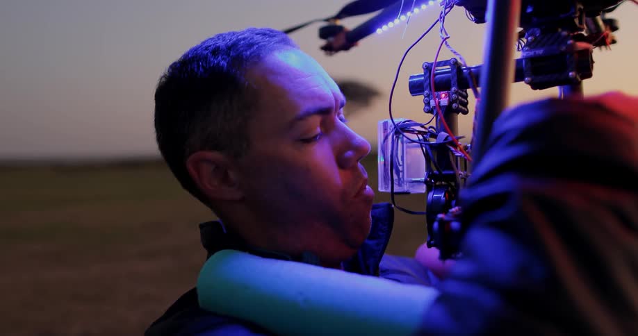 A man holds a drone in an open field at dusk