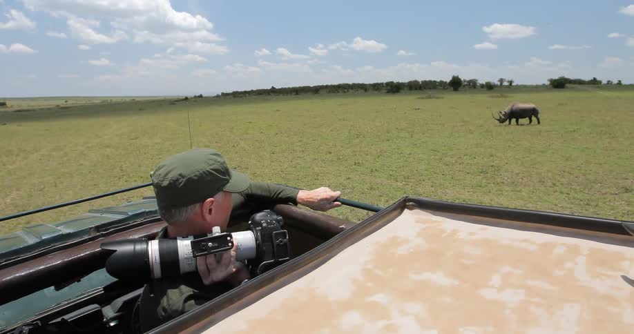 A man holding a camera in a safari jeep watches a rhino