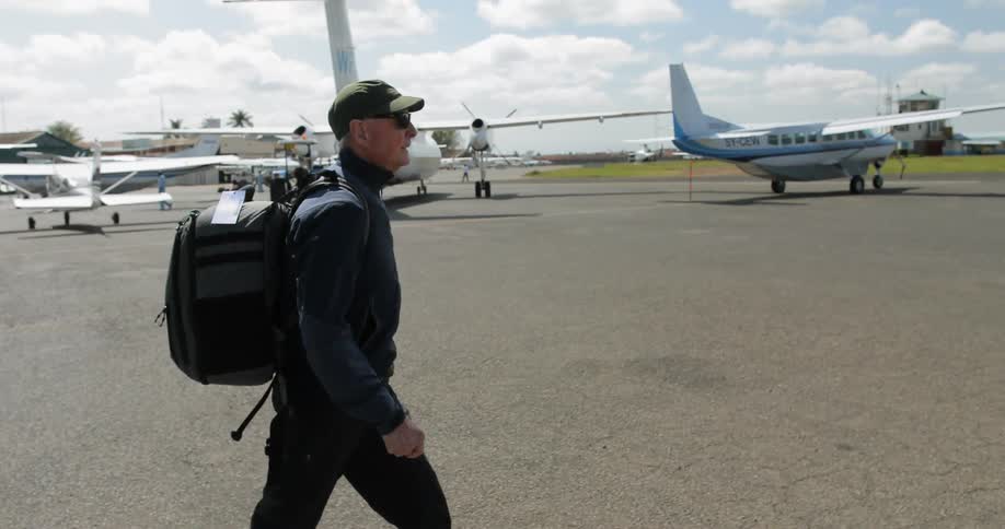 An elderly man walking across the tarmac near some small planes
