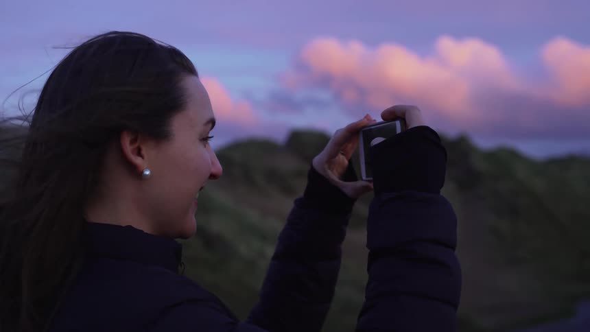 A woman uses her smart phone to record video of a windy hillside