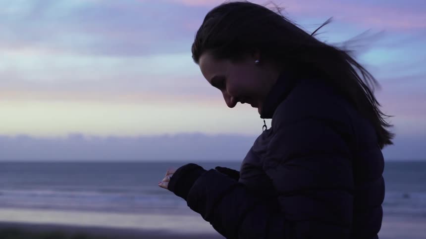 A white woman takes a selfie with her phone on the beach