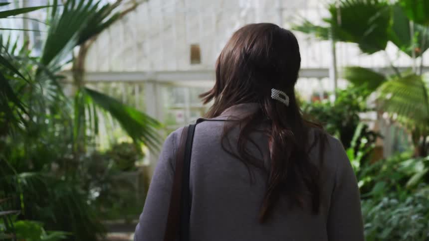 A woman walks through a greenhouse filled with a variety of tall green plants
