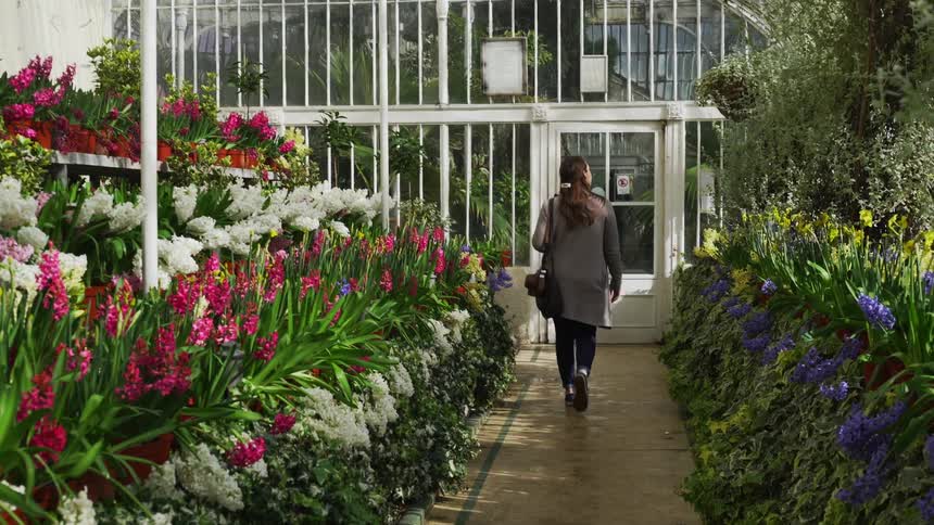 A woman walks through a greenery filled with flowers