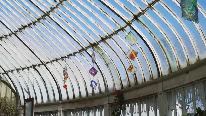 Interior of old greenhouse with hanging stained glass art and plants