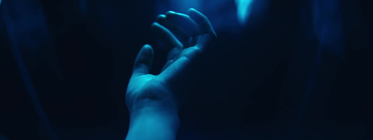 Hand stretches upward in shadowy roof tinted blue by colored light