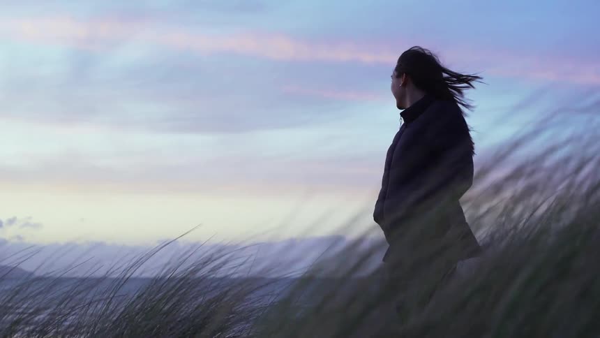 A woman stands and looks out towards the water