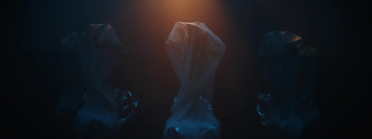 Three objects wrapped in plastic stand under lighting