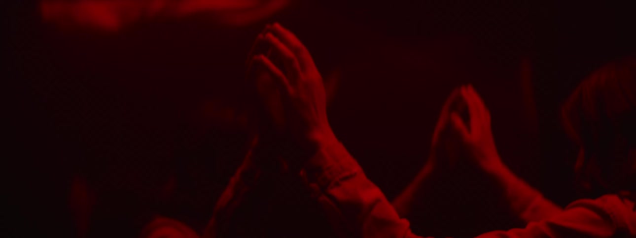 A teenager in a dark room holds her hands up against a mirror and looks in to it