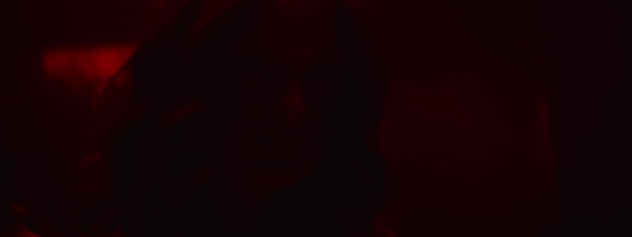 A woman standing in a dark room dimly lit with blood red lighting