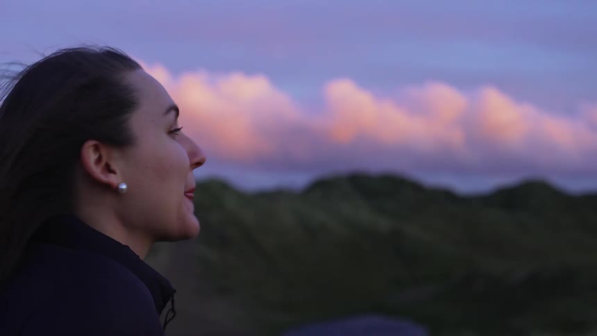 Woman looks at the mountains and smiles broadly at sunset on a windy day
