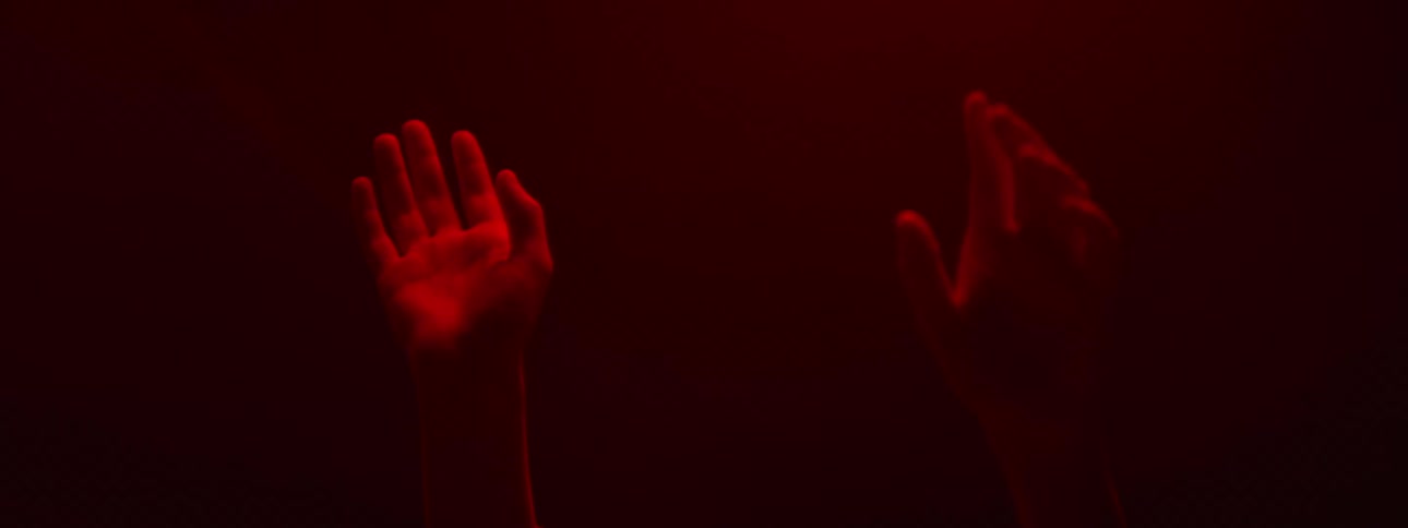 A person inside a room with red light raises with their hands raised up