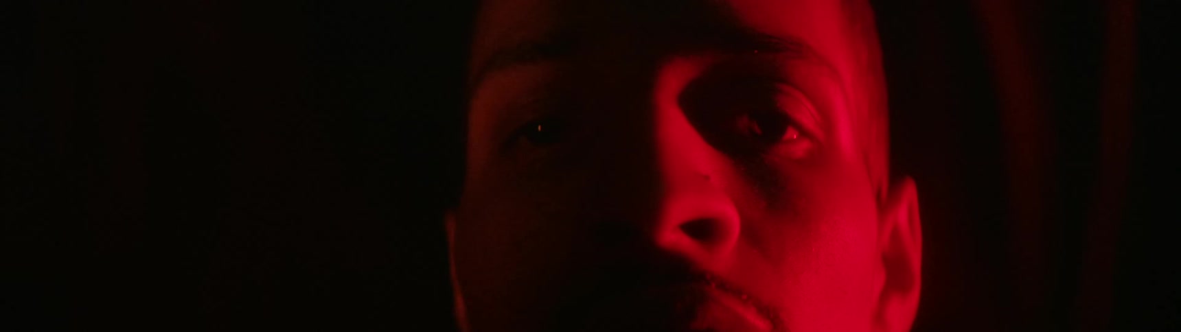 Man lit by a red light turns to face the camera