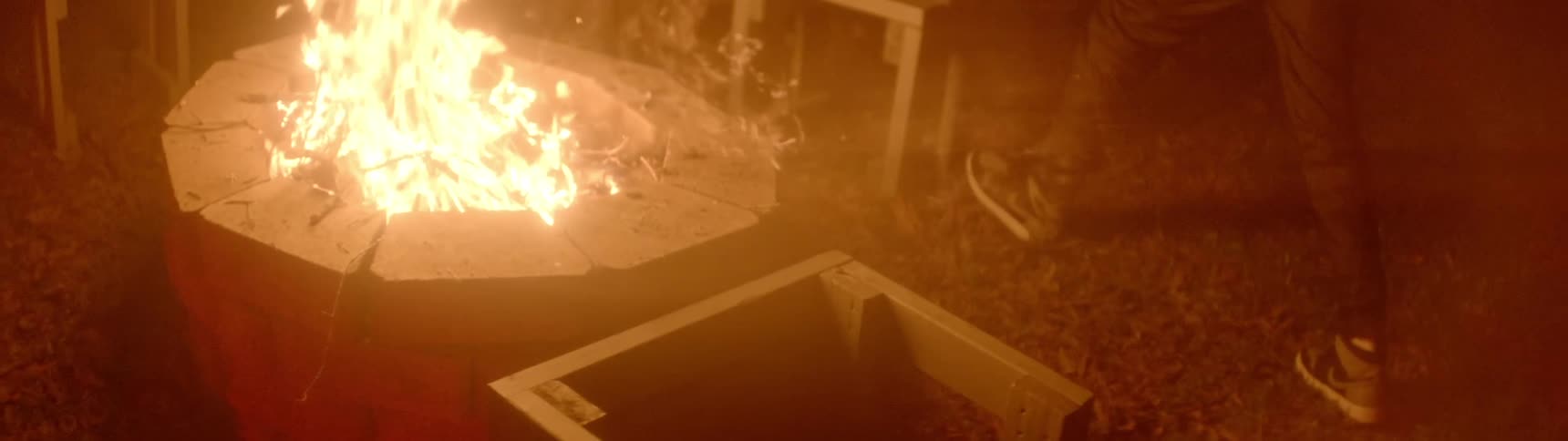 An angry black man flips over stools next to a roaring fire pit
