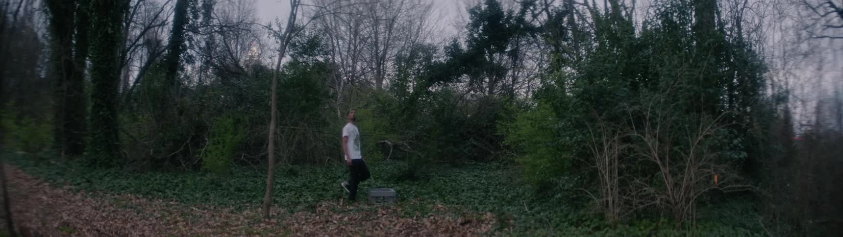 A white man stands on the edge of the woods and looks around