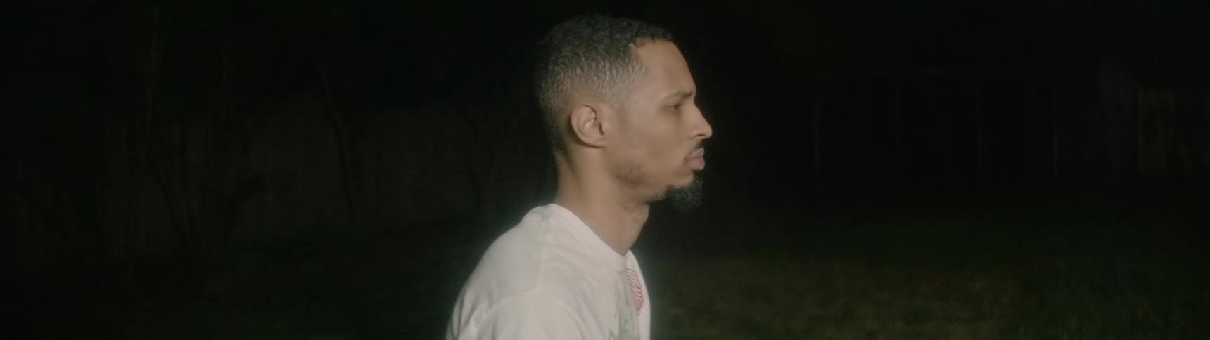 A black man stands in a yard at night as a light flashes on him