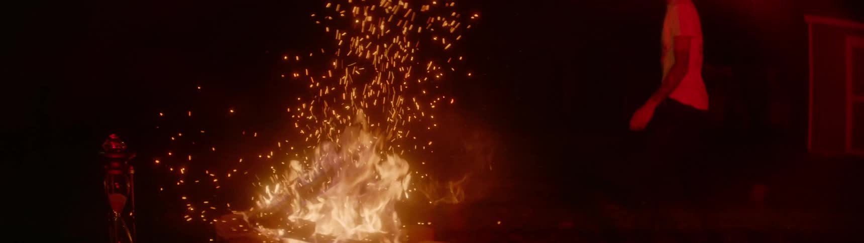 A black man throws a wooden stool on a fire burning in a fire pit