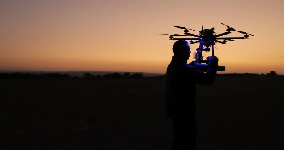 A man holds a drone with a flashing light at dusk