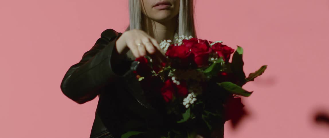 Young woman pulls rose from bouquet and throws it at camera