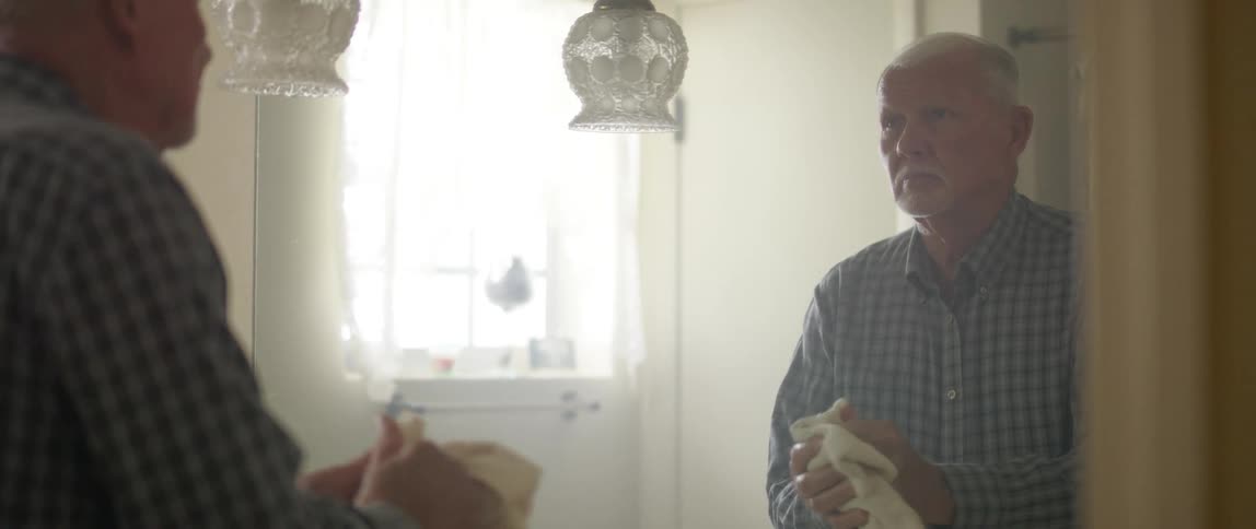 Elderly man freshens up and looks in the mirror in the bathroom