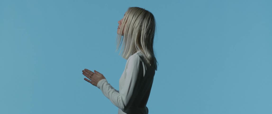 A white teenager stands and raises her hands as if in prayer
