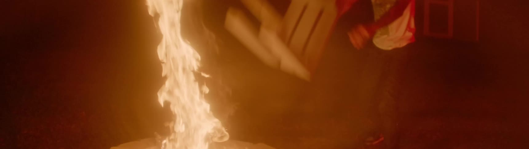 A man throws a wooden stool on a fire in a fire pit