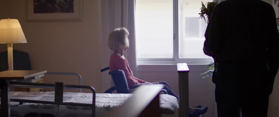 A man walks in to a patient room toward a woman in a wheel chair holding flowers