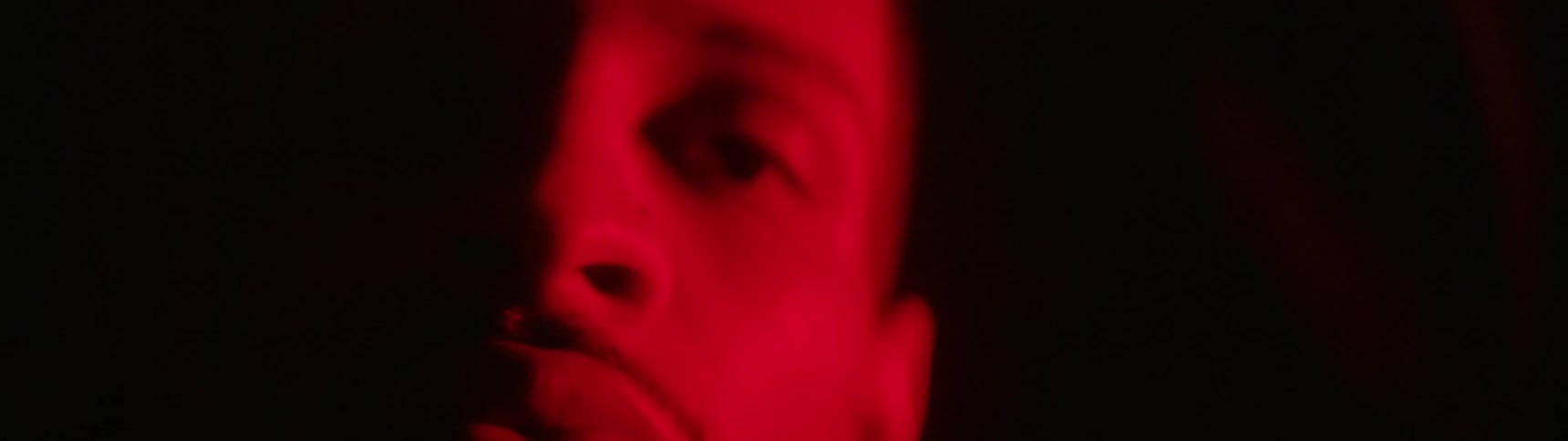 A red light shines on the face of a man standing in a dark room