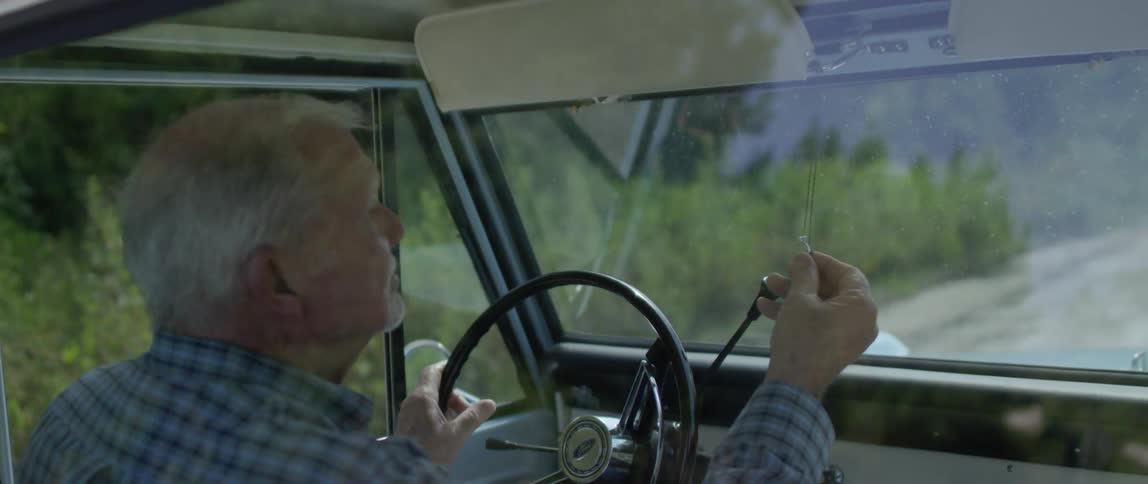 Older man looking at ring on chain hanging from rearview mirror in classic truck