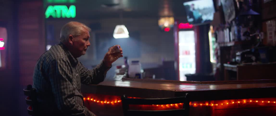 An elderly man sits at a bar and has a drink