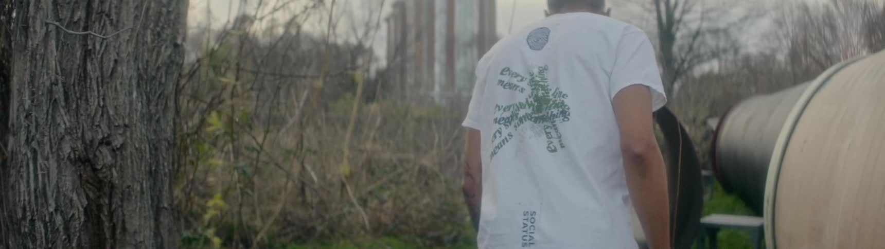 A black man walks up to sewer pipes lying in a forest