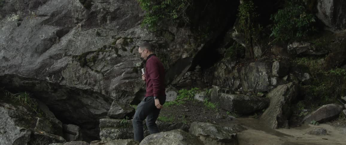 A man walks down rock steps in a canyon while holding a drink